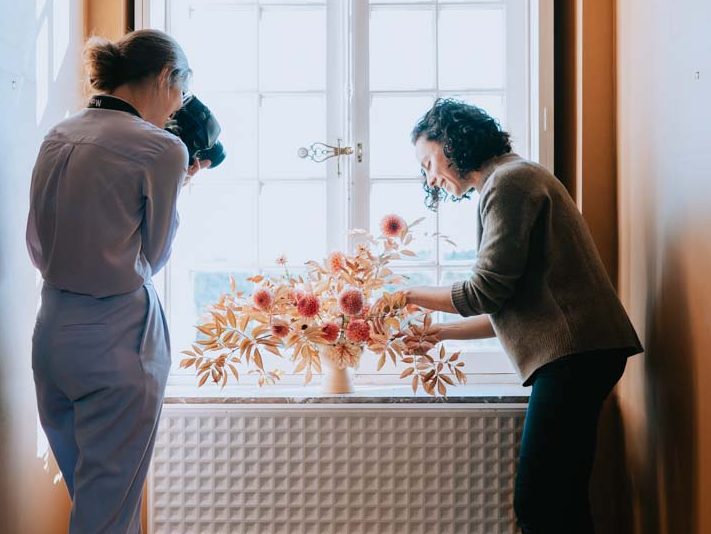 Photographe argentique professionnelle réalise une image d'une nature morte avec une composition florale posée sur le rebord d'une fenêtre.