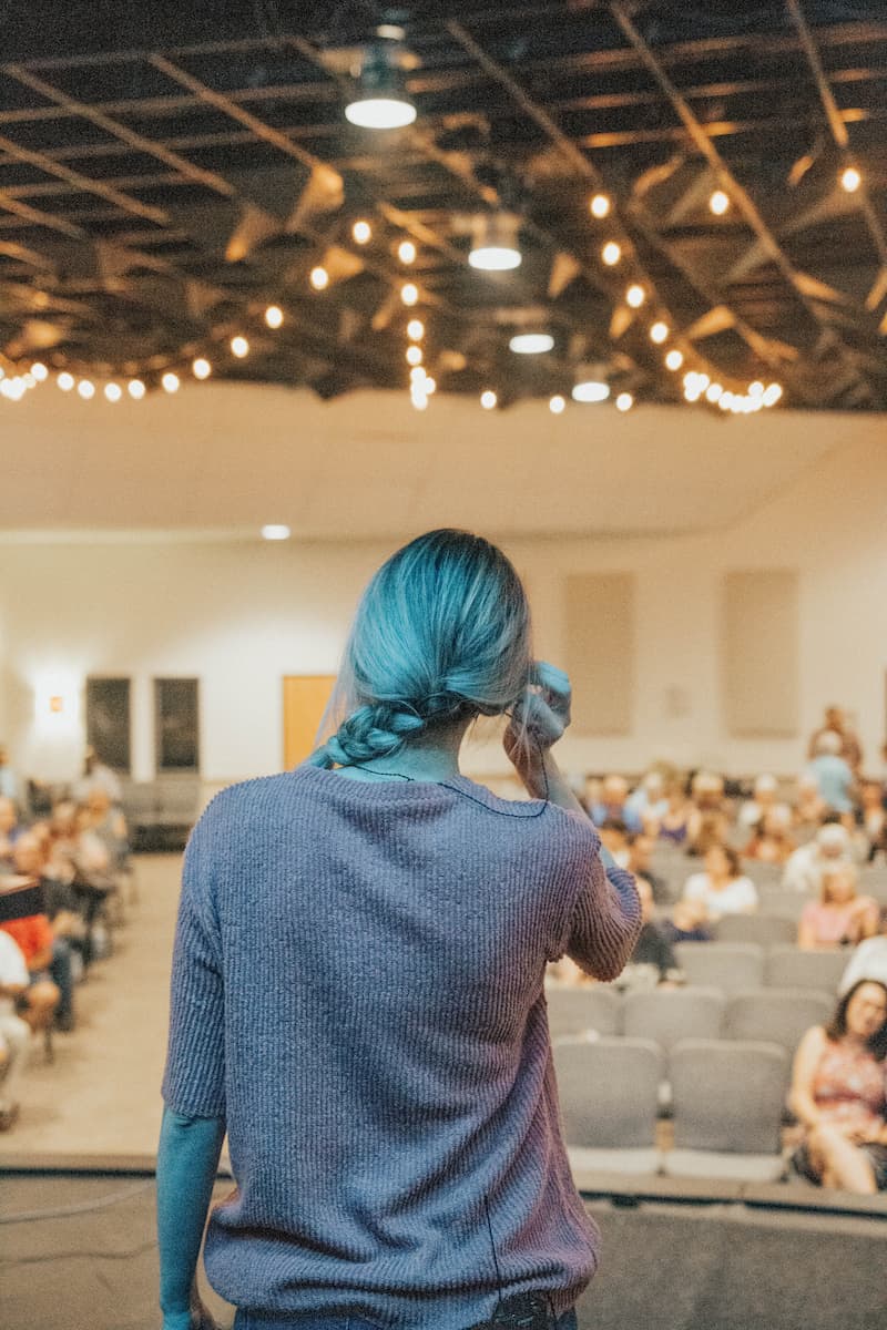 Portrait de dos d'une jeune femme devant un auditoire.